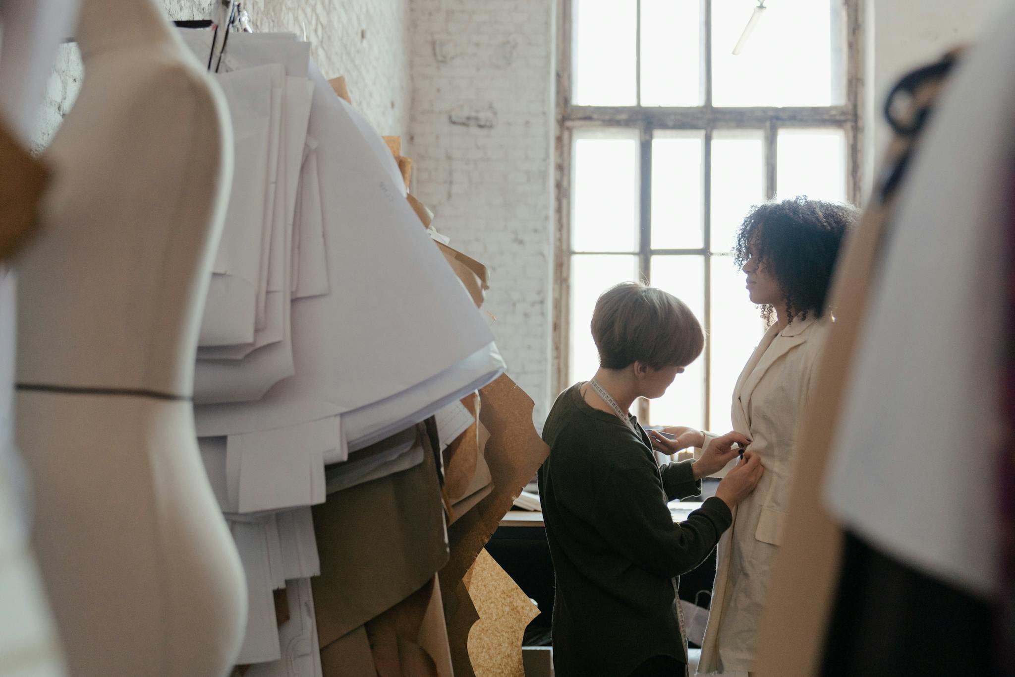 A tailor adjusts a garment on a model in a bright, modern fashion atelier.